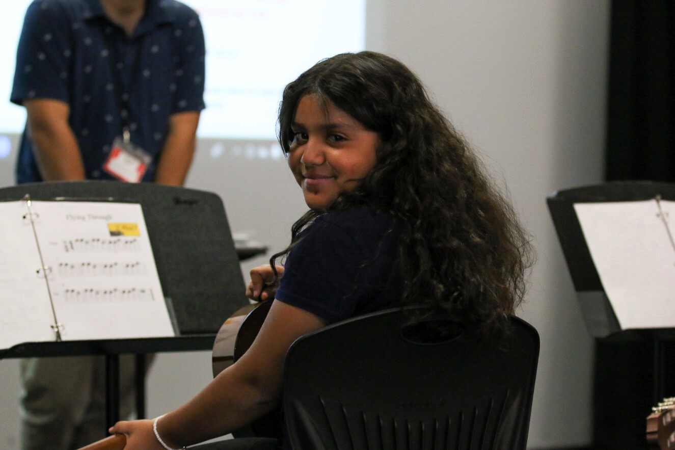 A girl turns to smile during guitar class.