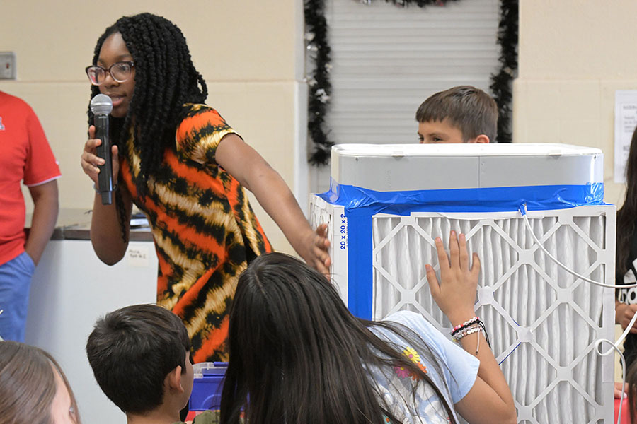 A teen girl shows the air filter she made to students