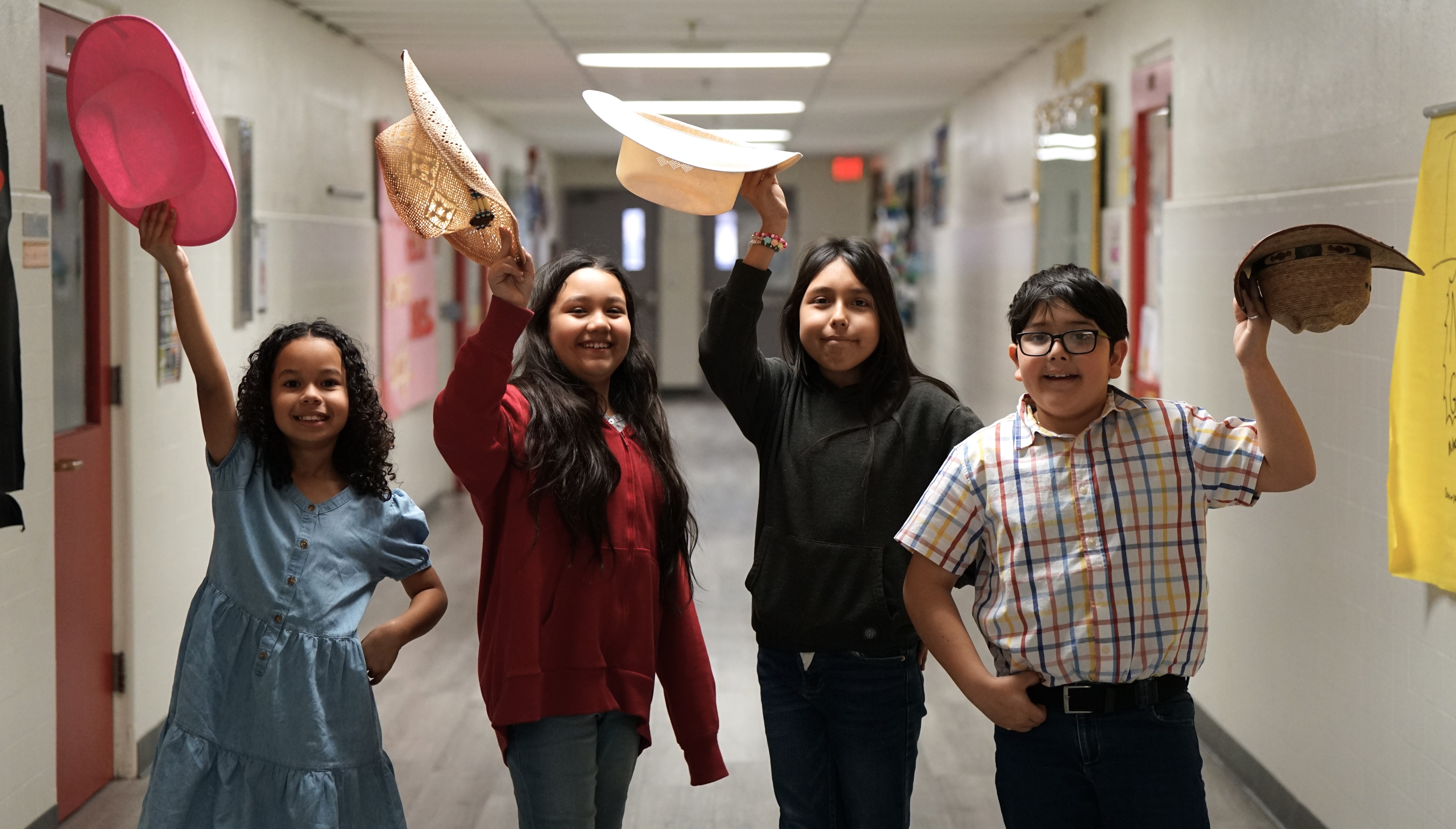 Four students hold up their cowboy hats in the hallway