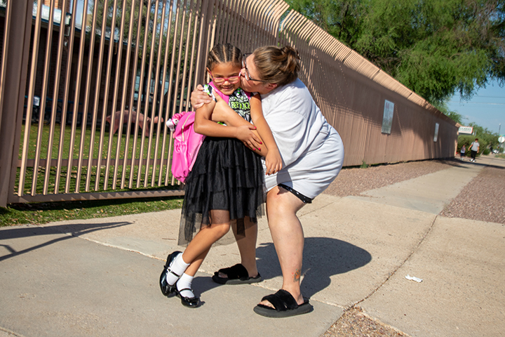 A mom hugs her daughter tightly outside the school courtyard