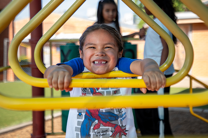 A little boy has a big smile as he plays on yellow monkey bars