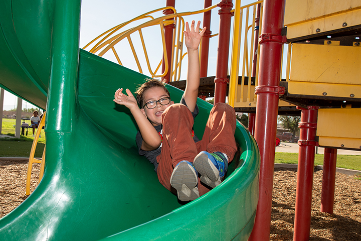A boy smiles as he goes down a green twisty slide