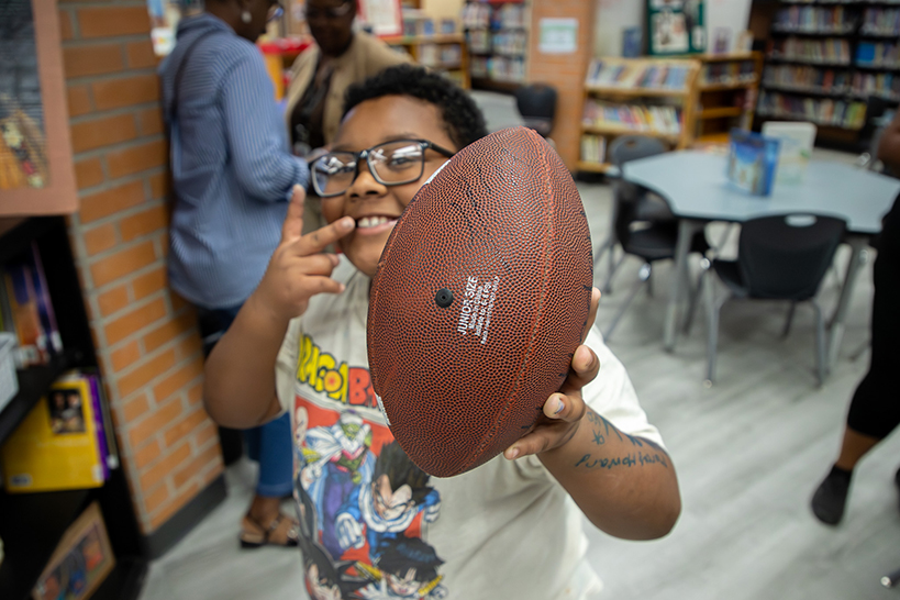A little boy in glasses smiles as he holds up his signed football