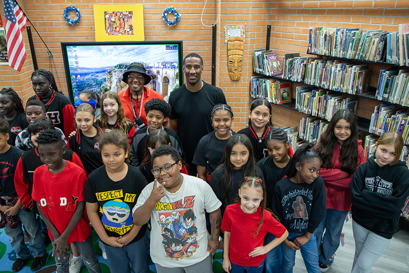 A man smiles with a class of students in the library
