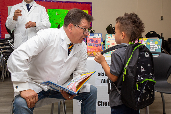 A man in a white lab coat and glasses reads from a picture book to a young boy