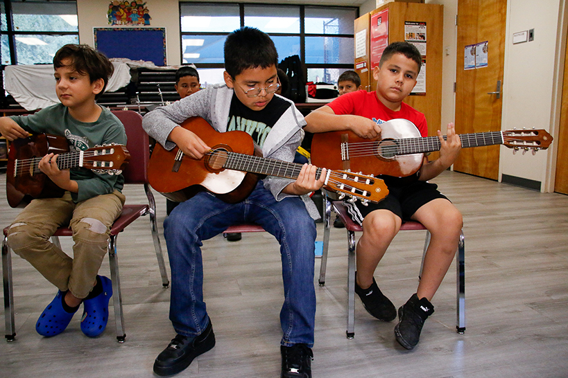 Three boys sit in chairs playing acoustic guitars