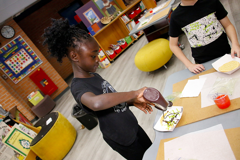 A girl pours chocolate syrup on her culinary creation