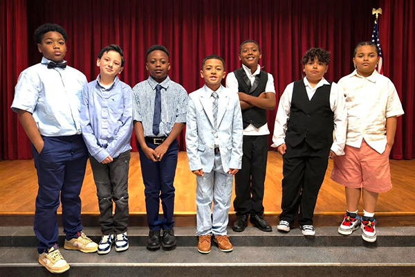 A group of young boys dressed in nice clothes stand on stage