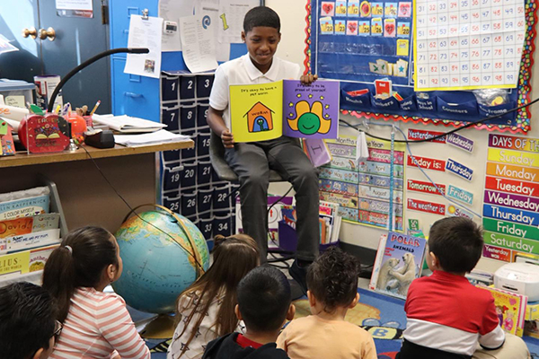 A preteen boy reads to a group of young kids