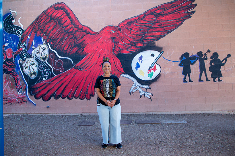 A woman stands in front of a red hawk mural
