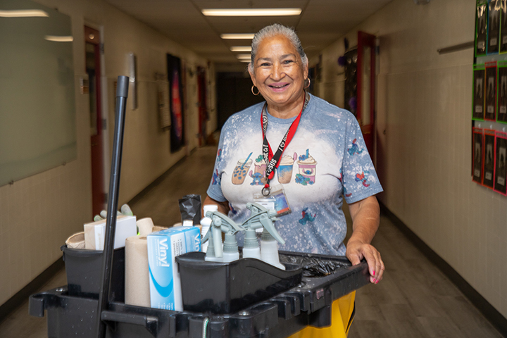 A woman smiles behind a janitorial cart